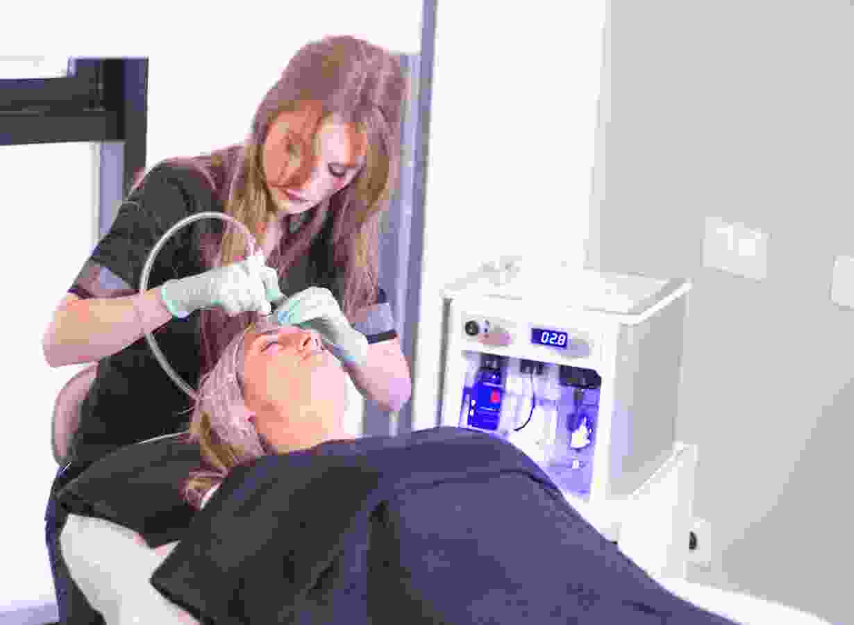 A woman is using an electric device to treat a man 's face.